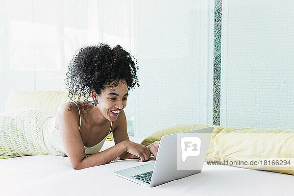 Happy woman lying on bed and using laptop at home