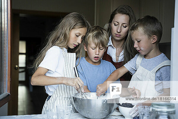 Woman looking at children preparing batter in kitchen