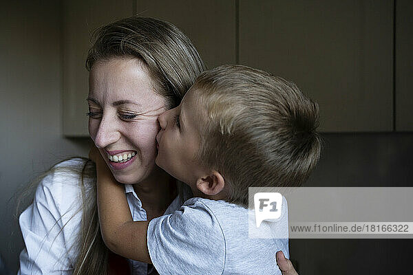 Boy kissing happy mother in kitchen