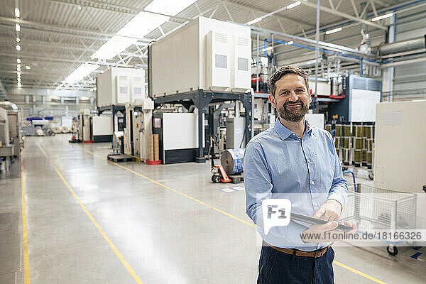 Smiling businessman with tablet PC standing in industry