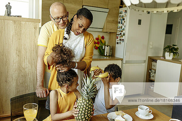 Smiling man embracing woman tying daughter's hair sitting by brother at home