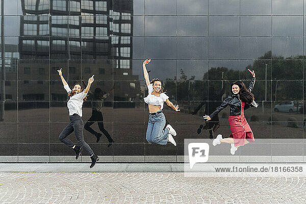 Cheerful friends jumping in front of glass wall