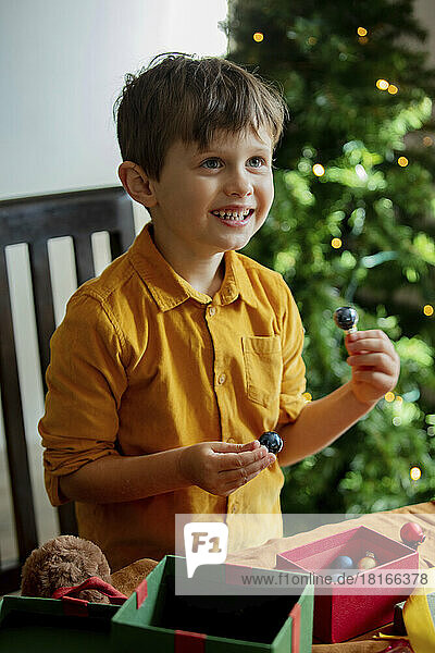 Happy boy with Christmas baubles and gifts at table