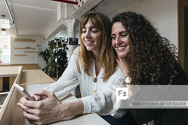 Two happy businesswomen sharing mobile phone in office