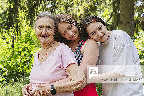 Lächelnde ältere Frau mit Tochter und Enkelin  die sich im Park umarmen