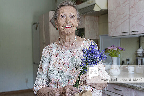 Smiling senior woman with bunch of lavender flowers at home