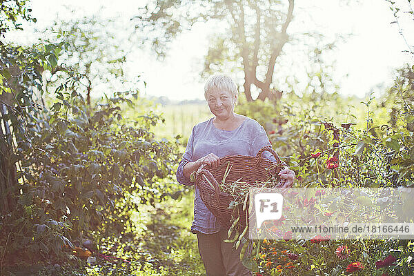 Smiling mature woman with basket standing amidst plants