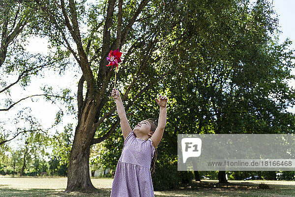 Mädchen mit erhobenen Armen hält Windradspielzeug im Park