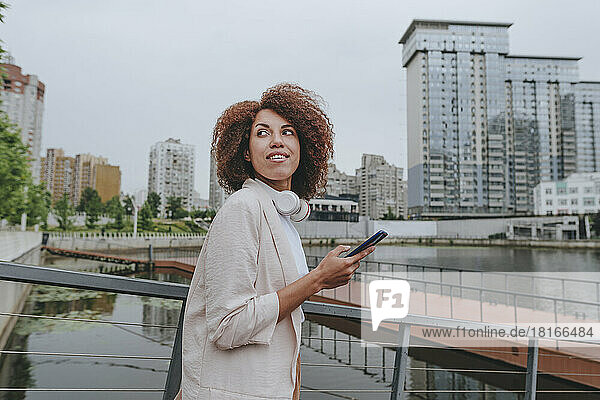 Young businesswoman walking with smart phone by railing
