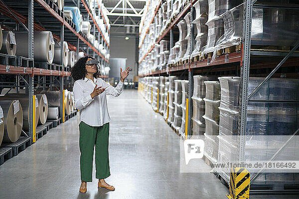 Businesswoman wearing virtual reality simulator gesturing in aisle at factory