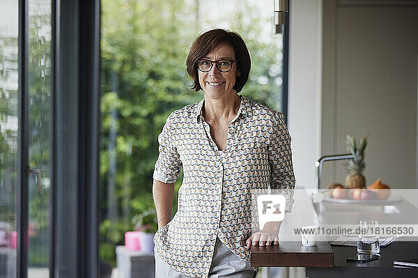 Happy senior woman wearing eyeglasses standing by kitchen island at home