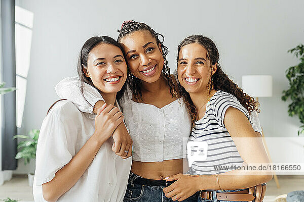 Happy multiracial roommates with arms around in living room