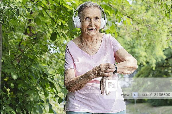 Happy senior woman with smart watch listening to music through headphones in park
