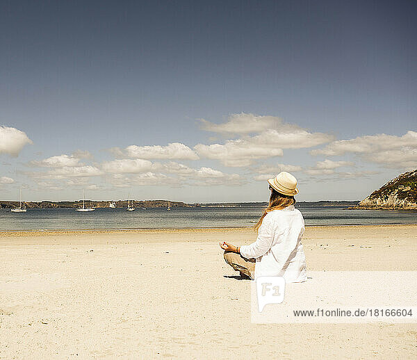 Woman wearing hat practicing meditation at beach on sunny day
