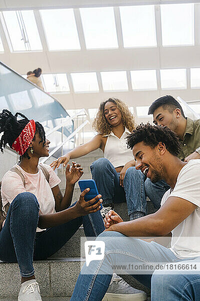 Multiracial friends watching smart phone and laughing on staircase