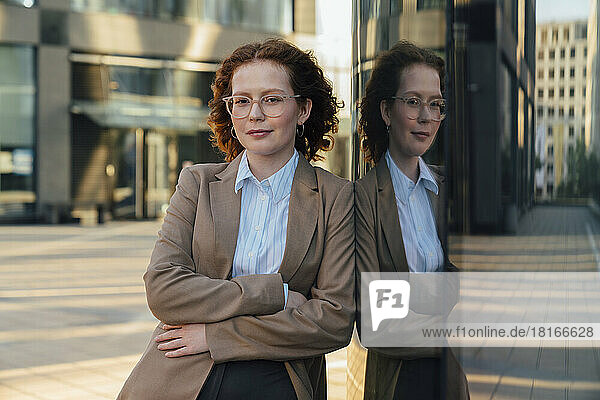 Confident beautiful businesswoman with eyes closed leaning on glass wall