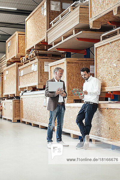 Businessman holding laptop talking to colleague standing in warehouse