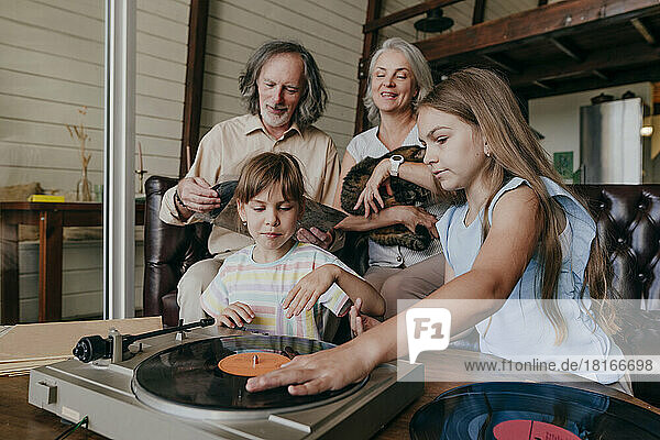 Enkelinnen spielen mit den Großeltern zu Hause Musik auf einem Vinyl-Plattenspieler