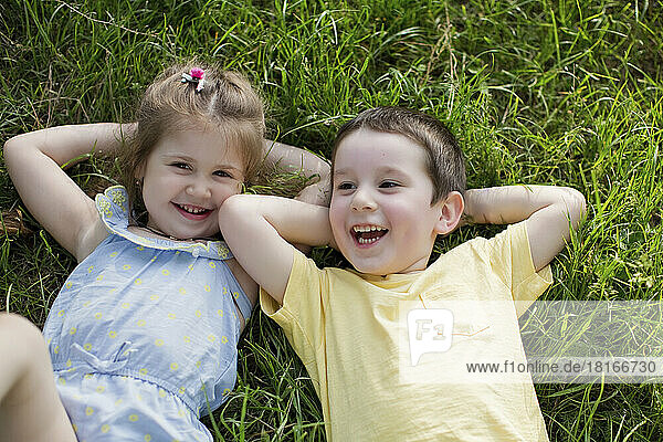 Happy boy with sister relaxing on grass at park