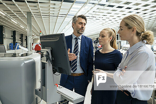 Mature businessman having discussion with colleagues over desktop computer in industry