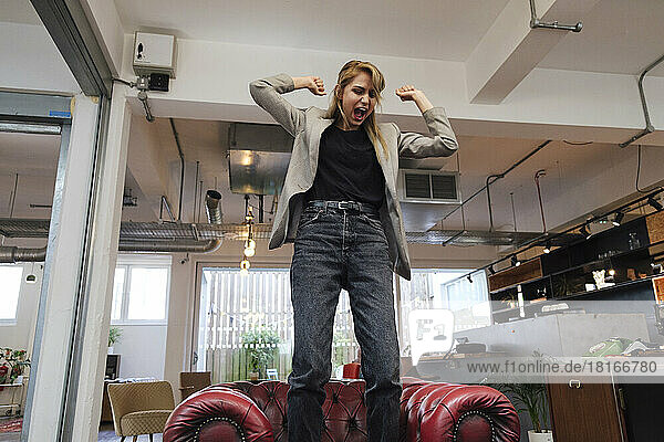Young businesswoman standing on armchair screaming with anger