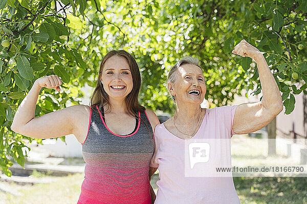 Aktive Seniorin lässt Muskeln spielen  während Fitnesstrainer im Park steht