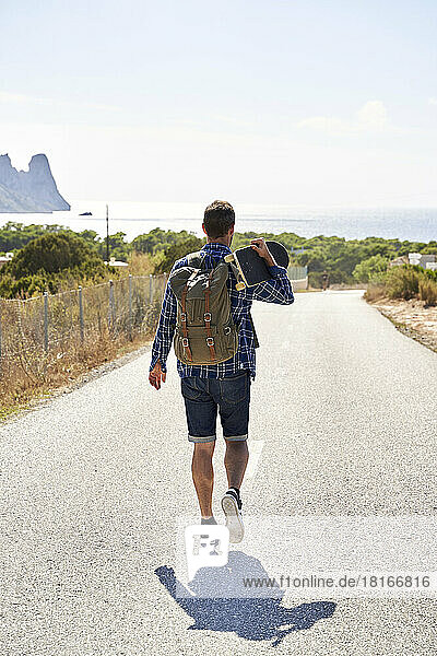 Man wearing backpack walking with skateboard on road