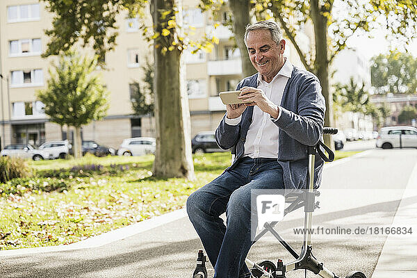 Happy senior man using smart phone sitting on mobility walker