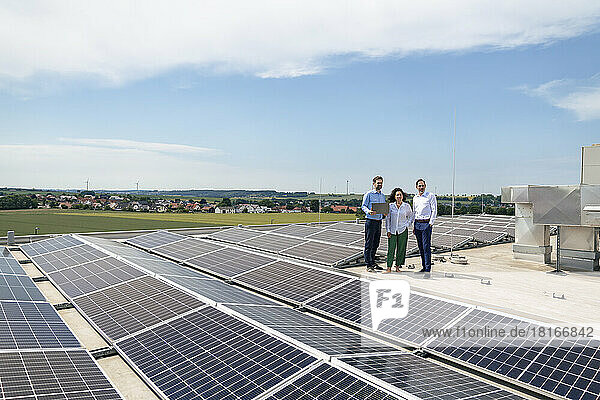 Businessman holding laptop standing with colleagues in front of solar panels