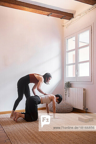 Young woman assisting friend practicing yoga at home