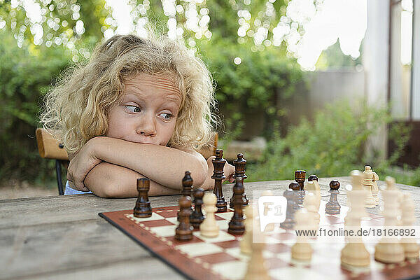 Thoughtful girl with blond hair looking at chessboard on table