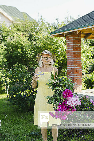 Woman holding pruning shears and flowers in garden