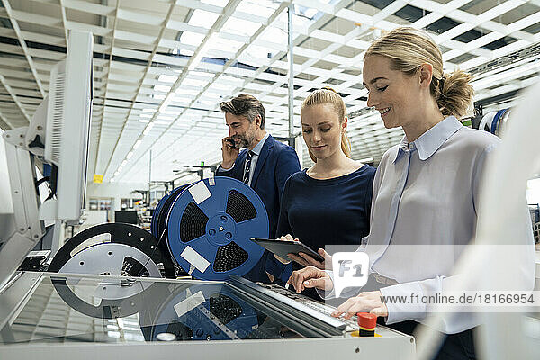 Smiling businesswoman operating machinery with colleagues standing by at industry