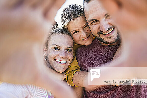 Laughing family embracing and looking through hands at camera