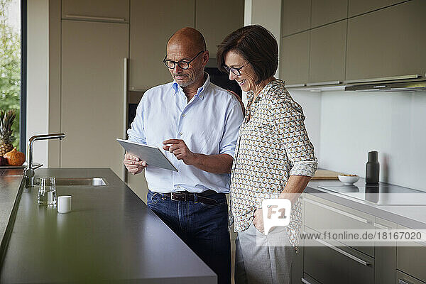 Glückliche Frau mit Mann  der zu Hause in der Küche einen Tablet-PC benutzt