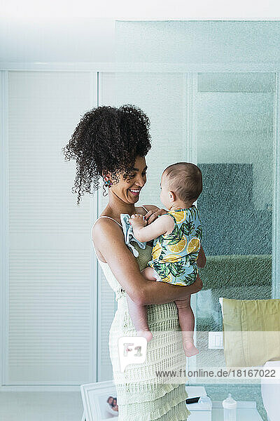 Happy woman carrying baby boy in bedroom at home