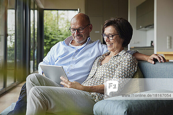 Glückliche ältere Frau mit Mann  der zu Hause einen Tablet-PC auf dem Sofa benutzt