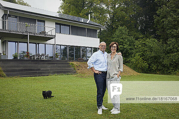 Glücklicher älterer Mann und Frau mit Katze stehen vor dem Haus