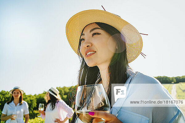 Lächelnde Frau mit Hut und Weinglas an einem sonnigen Tag