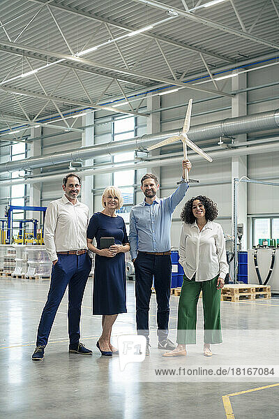 Mature businessman holding wind turbine model standing by colleagues in industry