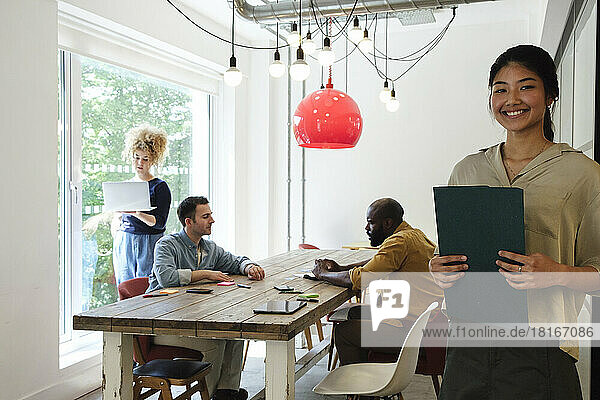 Smiling woman leaning aginst wall while business people work together