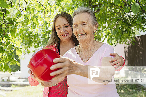 Smiling fitness instructor teaching exercise with ball to senior woman in park