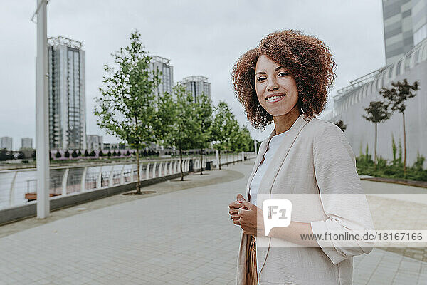Smiling businesswoman with Afro hairstyle standing at promenade