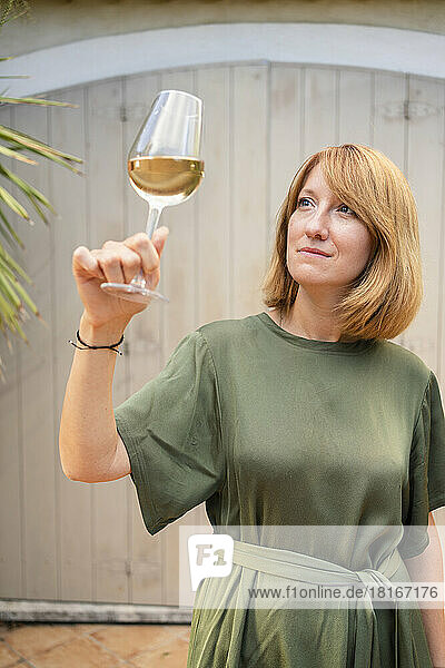 Thoughtful mature woman looking at white wine in front of wall