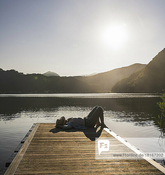 Woman lying on jetty over lake by mountains