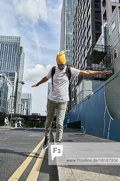 Man with arms outstretched balancing on edge of footpath