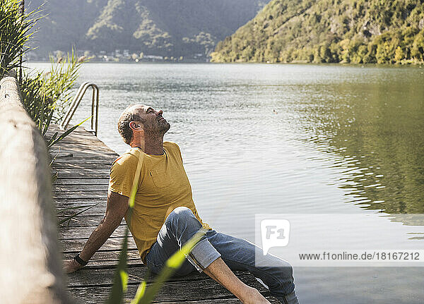 Mann entspannt sich mit geschlossenen Augen auf Steg am See