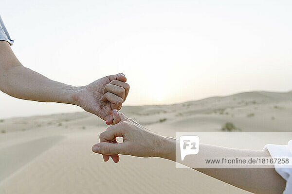 Hands of couple holding little fingers in desert at sunset