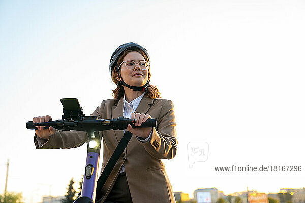Smiling businesswoman with helmet riding electric push scooter