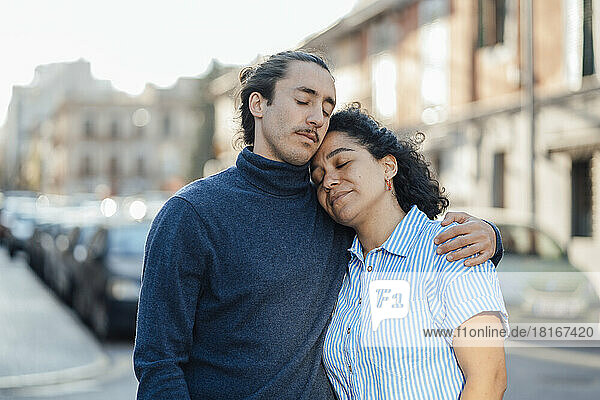 Junger Mann umarmt seine Freundin mit geschlossenen Augen auf der Straße